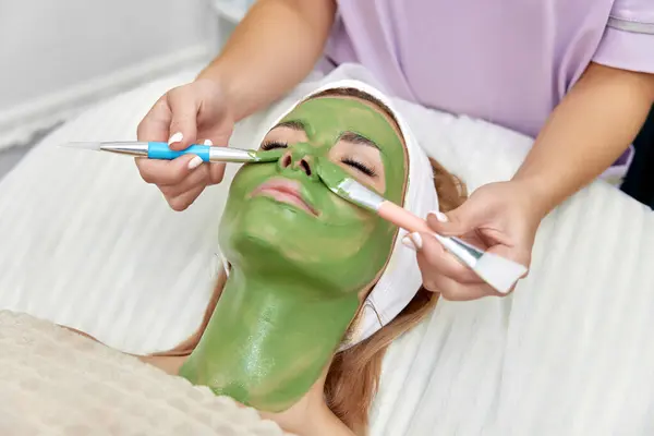 female beautician applies the mask to the face of beautiful woman in the spa salon. facial skin care