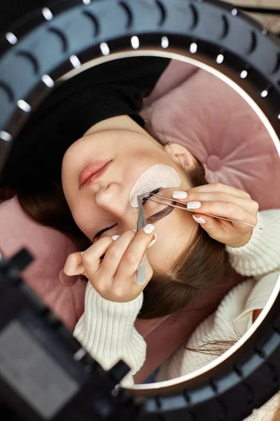 专业美容师用镊子为环灯下的美女做睫毛伸展 顶视图 — 图库照片