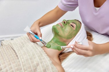 Kadın güzellik uzmanı maskesini güzellik salonundaki güzel kadının yüzüne takıyor. yüz bakımı