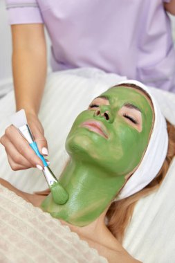 Kadın güzellik uzmanı maskesini güzellik salonundaki güzel kadının yüzüne takıyor. yüz bakımı