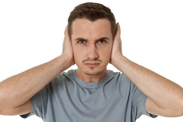 caucasian man in t-shirt covers ears with hands on white background