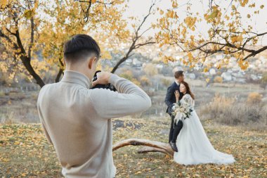 Profesyonel düğün fotoğrafçısı sonbaharda gelin ve damadın fotoğraflarını çekiyor.