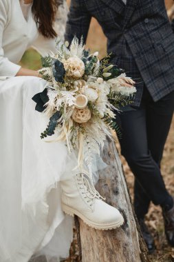 Gelin ve damat beyaz çizmeler giyerek güzel bir sonbahar buketi tutuyorlar..