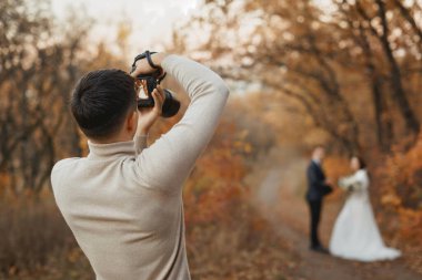 Profesyonel düğün fotoğrafçısı sonbaharda gelin ve damadın fotoğraflarını çekiyor.