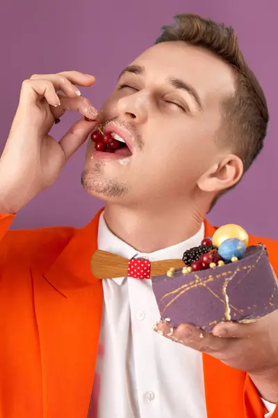 handsome birthday man in orange jacket eating cake on purple background