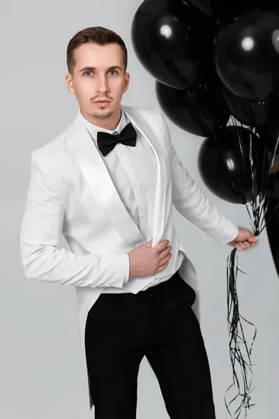 elegant caucasian man in white suit tuxedo with black air balloons on white background.