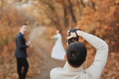 Profesyonel düğün fotoğrafçısı sonbaharda gelin ve damadın fotoğraflarını çekiyor.