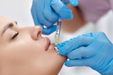 Kozmetik uzmanı güzel bir kadının dudaklarını büyütmek için iğneler yapar. Prosedür dudak büyütme