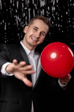 Siyah ceketli, arka planında kırmızı balon olan beyaz bir adam. Yeni yıl partisi
