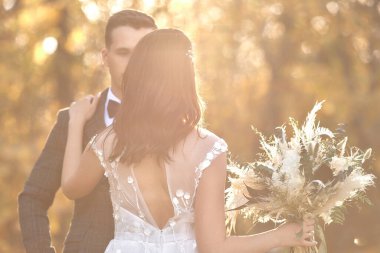 Beyaz gelinlik ve damat giymiş güzel gelin güneşli bir günde doğal arka planda dikiliyor. Boşluğu kopyala
