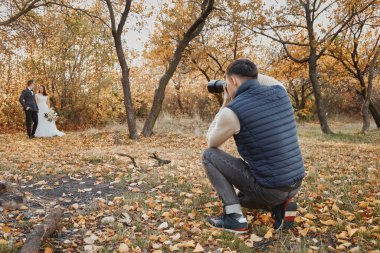 Profesyonel düğün fotoğrafçısı, gelin ve damadın dışarıda fotoğraflarını çekiyor.