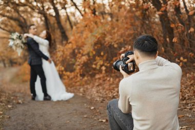 Profesyonel düğün fotoğrafçısı sonbaharda gelin ve damadın fotoğraflarını çekiyor.