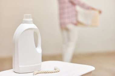 Çamaşır sepetindeki jel ya da kumaş yumuşatıcısını çamaşır sepetindeki bulanık kadının arka planına karşı. Model yap, boşluğu kopyala.