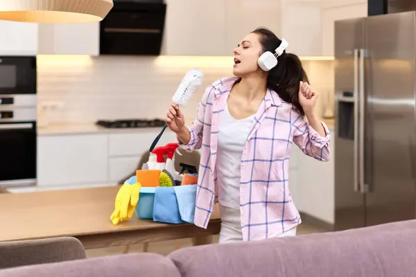young happy housewife woman singing and cleaning her home, girl enjoying domestic work.