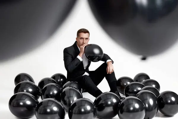 handsome man in black jacket blowing black air balloon on white studio background. birthday party