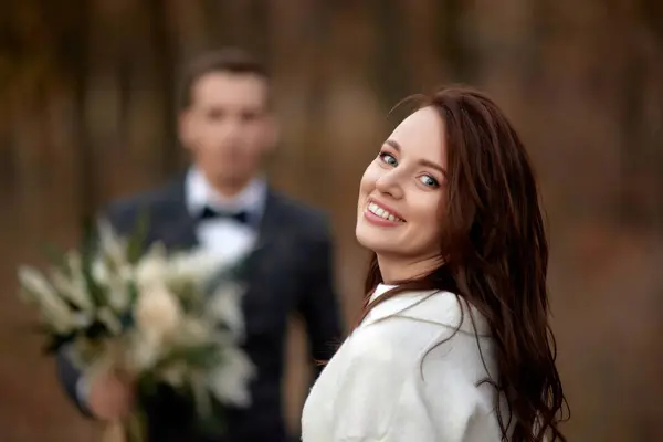 portrait of smiling bride and blur groom holding wedding autumn bouquet on the background