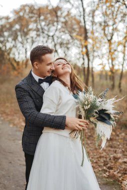 Gülümseyen gelin ve damat, sonbaharda dışarıda romantik anların tadını çıkarıyorlar.