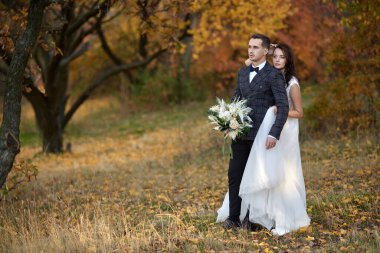 Beyaz gelinlik içinde güzel, şehvetli gelin ve damat düğünlerinde doğal arka planda sarılıyorlar.