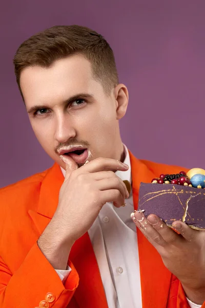 handsome birthday man in orange jacket holding cake looking at the camera being lovely and sexy on purple background