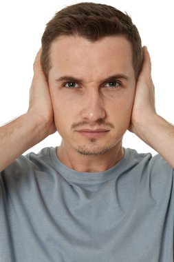 Tişörtlü beyaz adam kulaklarını beyaz arka planda kapatıyor.