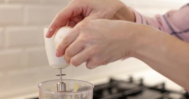 Yakın plan, dişi elleri yumurtayı kırıyor ve hamura ekliyor.