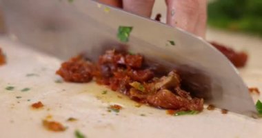 Kadın elleri büyük bir mutfak bıçağıyla kurutulmuş domatesleri kesiyor.