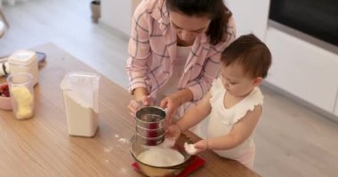 Mutlu anne ve küçük kız un toplayıp kaseye koyuyorlar. Küçük kız mutfakta unla oynuyor..