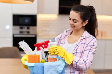 Lastik koruyucu sarı eldivenli kadın elinde kovayla deterjan ve bez parçaları tutuyor. ev işleri.