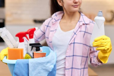 Lastik koruyucu sarı eldivenli kadın elinde kovayla deterjan ve bez parçaları tutuyor. ev işleri.