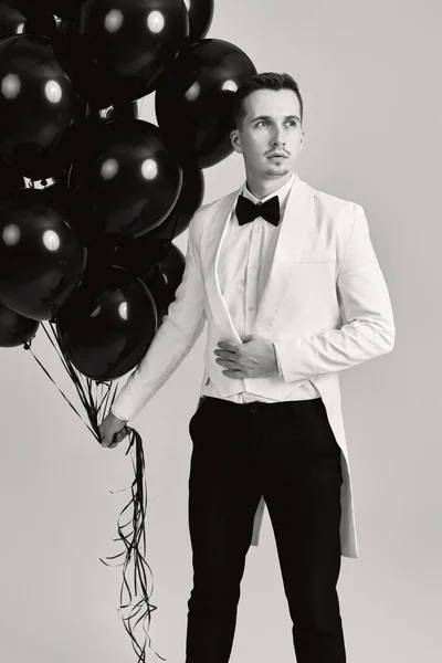 elegant guy in white suit tuxedo with black air balloons on white background. holiday celebration