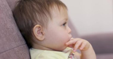 Çocuk kız elini emer, küçük bebek televizyon izler evde koçun karşısında oturur.