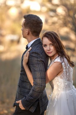 Beyaz gelinlik içinde güzel şehvetli gelin ve damat doğal arka planda dikiliyorlar.