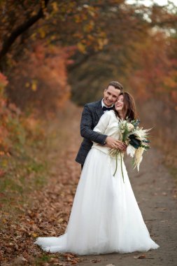 Beyaz gelinlik içinde güzel şehvetli gelin ve damat doğal arka planda duruyorlar.