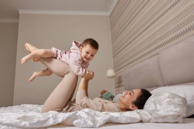 Mutlu Kafkasyalı anne gülüyor, sevimli bebek yetiştiriyor ve yatak odasında birlikte oynuyor.