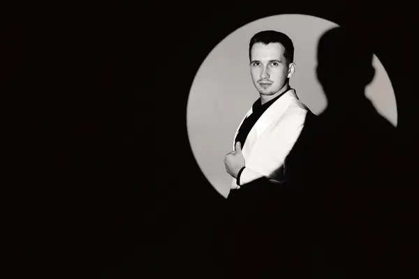 elegant man in white suit tuxedo in the circle of light, copy space. black and white