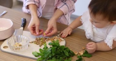 Kadın elleri mutfakta salata hazırlamak için fıstık kabuğu kırıyor, çocuk annesinin pişirmesine yardım ediyor.