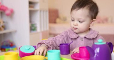 Küçük mutlu kız bebek odasında plastik çay fincanlarıyla oynuyor.