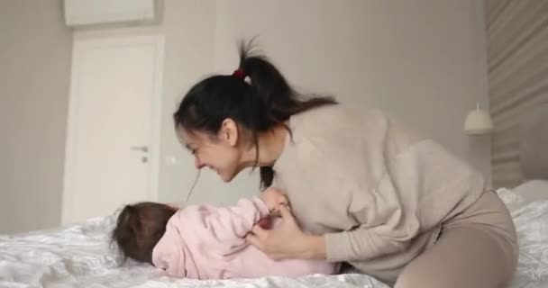 若い母親は彼女の笑う幼い赤ん坊の娘を朝の寝室でくすぐった — ストック動画