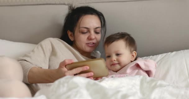母と子供はスマートフォンで遊んで 自宅の寝室のベッドで笑っているモバイルスクリーンを見て — ストック動画
