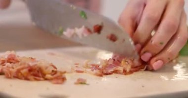 Kadın elleri büyük bir mutfak bıçağıyla domuz pastırması kesiyor.