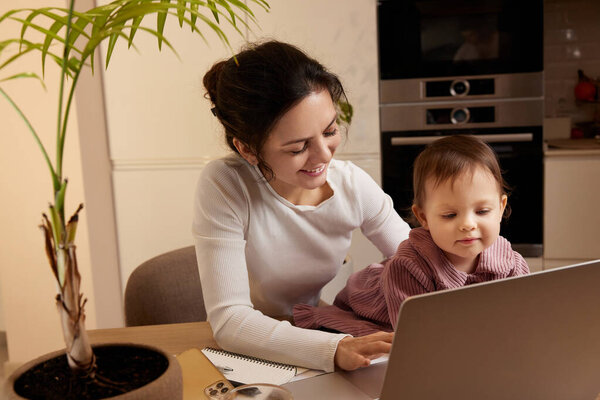 Cheerful woman working at home with her little child daughter