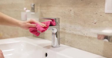 Yakın plan. Pembe bez kaplı kadın eli banyoda beyaz lavaboda musluğu yıkıyor.