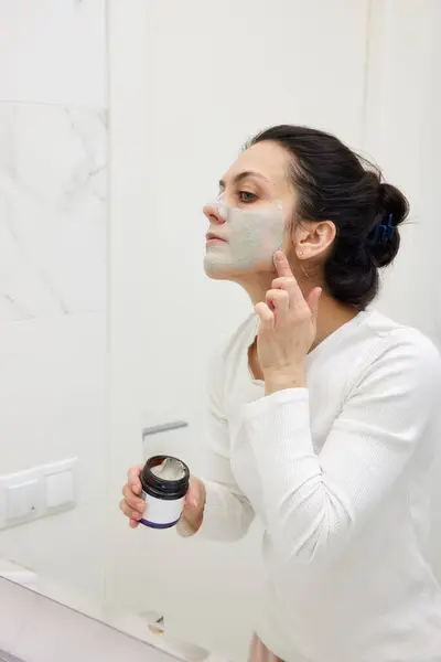 Kaukasische Frau Schaut Spiegel Und Trägt Gesichtsmaske Weiß Badezimmer Auf Stockfoto