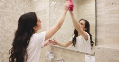 Kıvırcık ev kadını banyoda ayna yıkıyor. Temizlik kavramı.