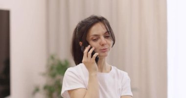 Gülümseyen beyaz kadın evde telefonla konuşuyor..