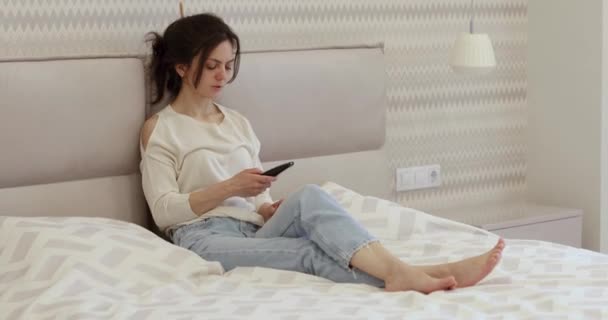 Женщина Сидит Кровати Смотрит Телевизор Помощью Пульта Дистанционного Управления Спальне — стоковое видео