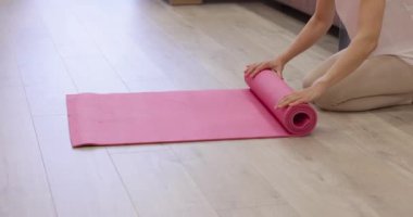 Kadın pembe yoga minderini kıvırıyor. Yakın plan. fit beyaz kadın evdeki oturma odasında egzersiz yogası yaparak egzersiz yapıyor.