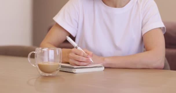 若い女性がホワイトノートに書き込み 自宅でコーヒーを飲む — ストック動画
