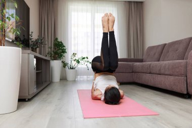 spor kadın sırt üstü uzanmış pembe paspasın üzerinde vücut ve bacakları kaldırarak evde çalışıyor.