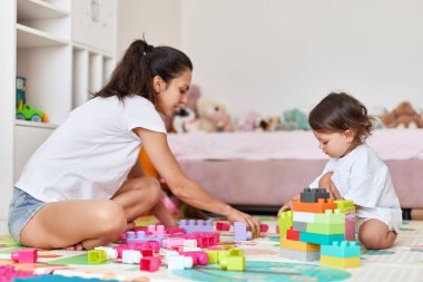 Sevimli kız ve sevgili annesi çocuk odasında oyuncak tuğlalarla oynuyorlar.